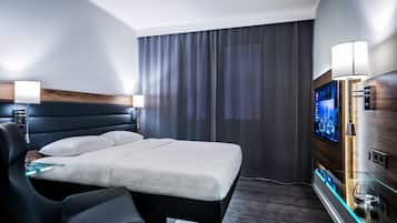 A modern hotel room with a large bed, a desk, a chair, a TV, and a lamp.