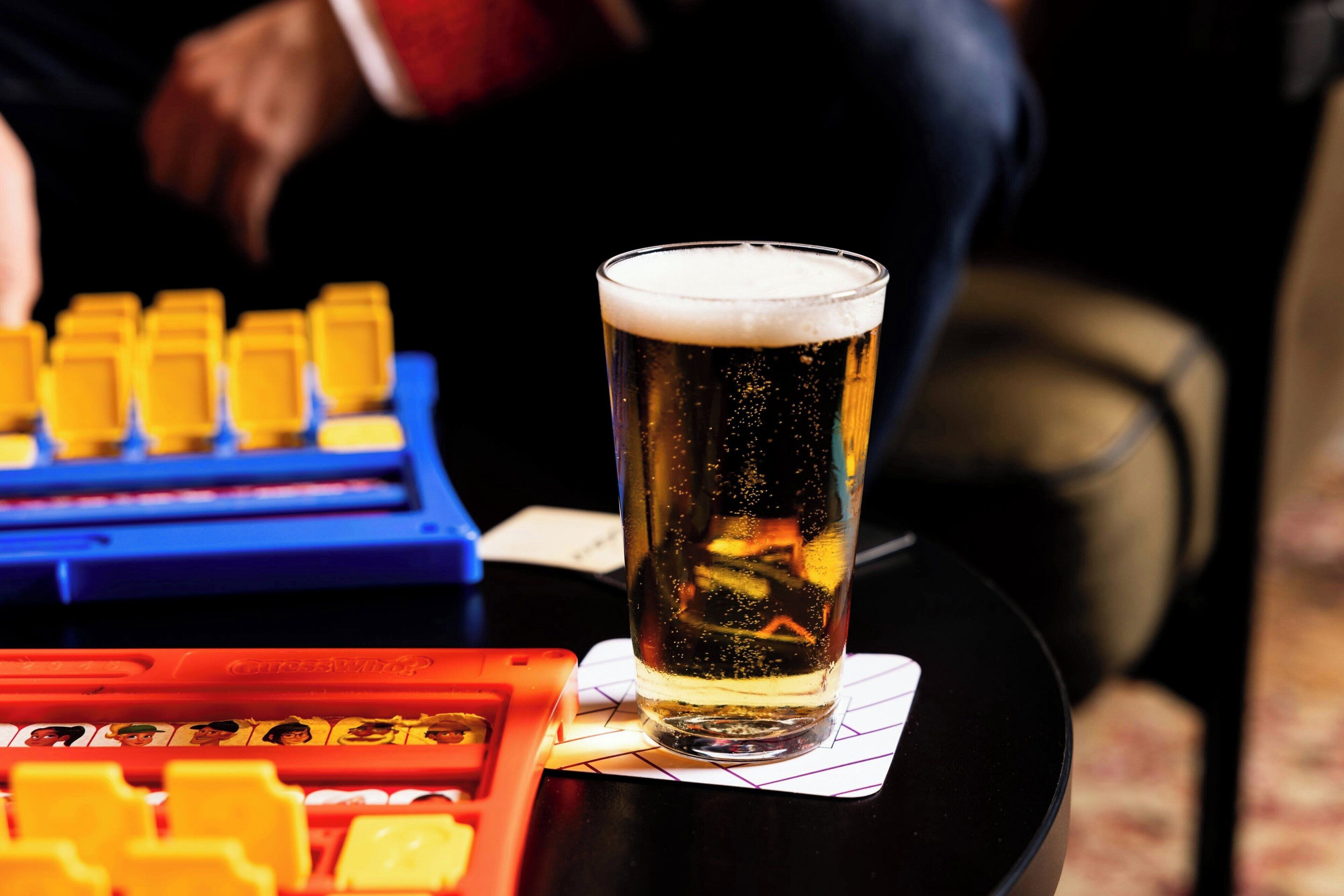 A glass of beer on a coaster with a game board in the background.