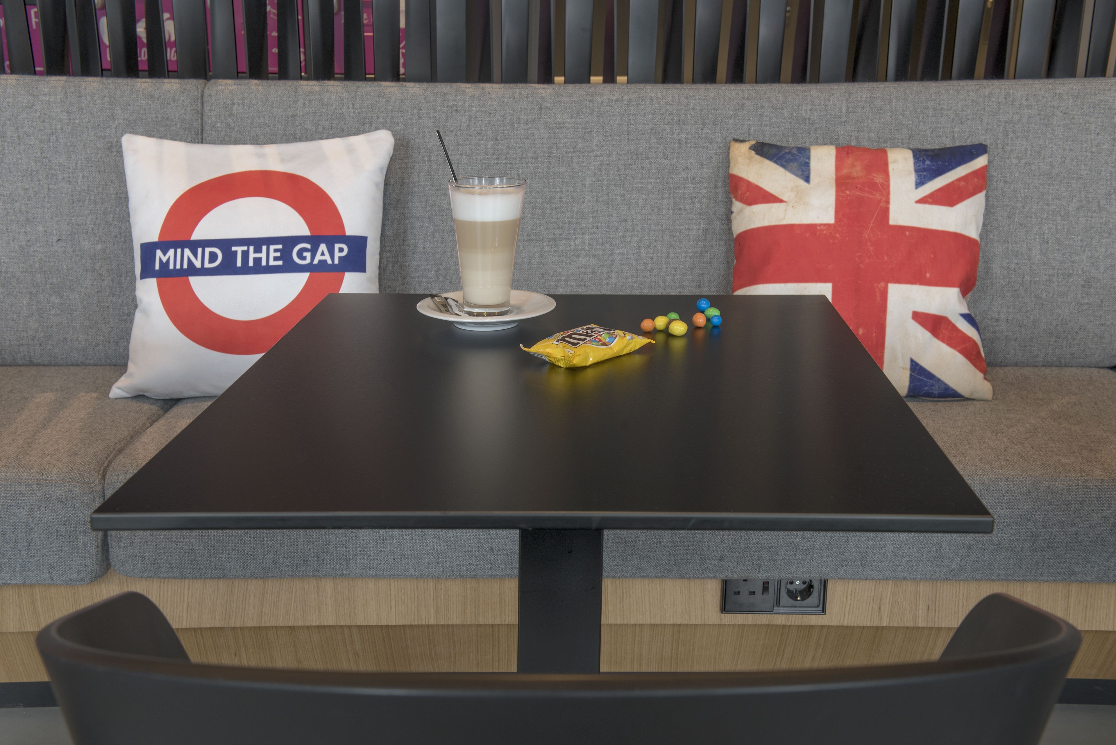 A table with a drink, snacks, and a cushion with a Union Jack design.