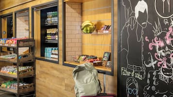A store interior with shelves stocked with snacks, a display of bottled beverages, and a chalkboard with a cat illustration.