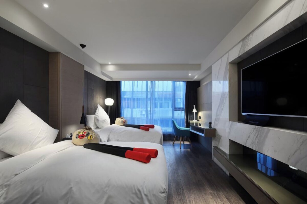 A modern hotel room with two beds, a TV, a desk, and a large window.