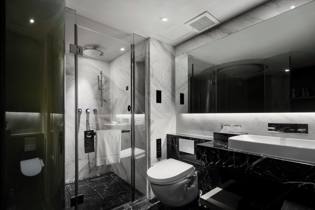 A modern bathroom with a glass-enclosed shower, a toilet, and a sink with a marble countertop.