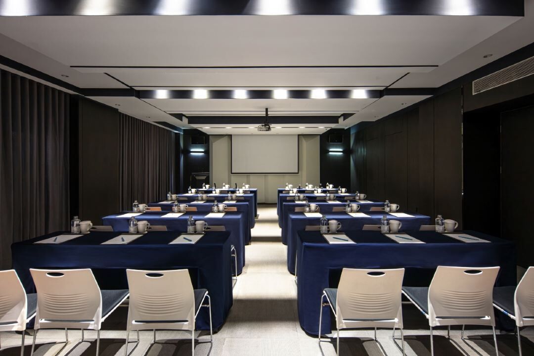 A conference room with multiple tables, chairs, and a projector screen.