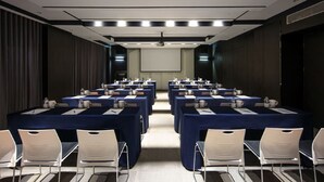 Une salle de conférence équipée de plusieurs tables, de chaises et d’un écran de projection.