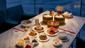 Une table dressée avec divers plats, notamment des dim sum, des fruits et un bol de soupe, dans un espace de restauration moderne offrant une vue agréable.
