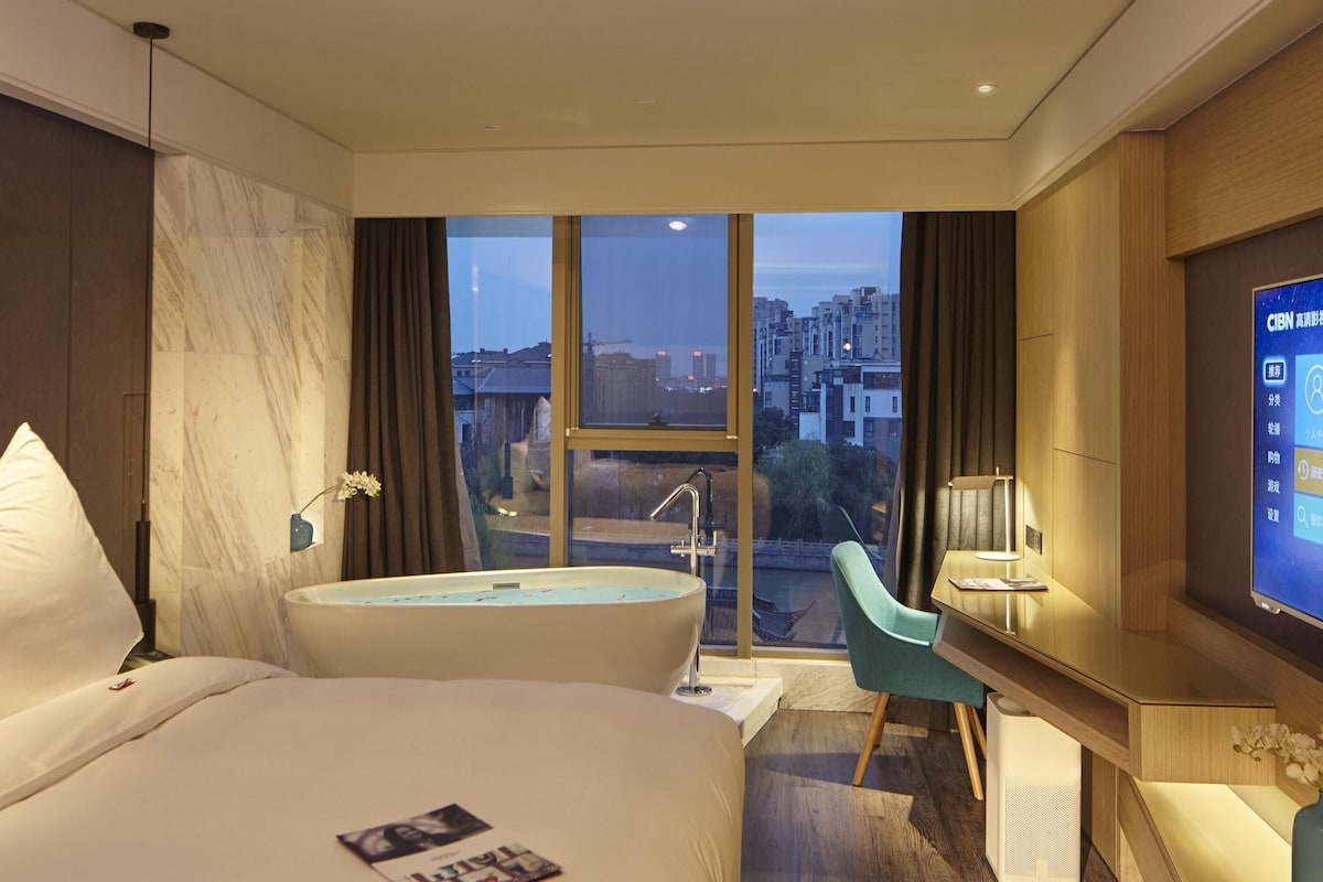 Ein modernes Hotelzimmer mit einem großen Bett, einer Badewanne, einem Schreibtisch und einem Fernseher.