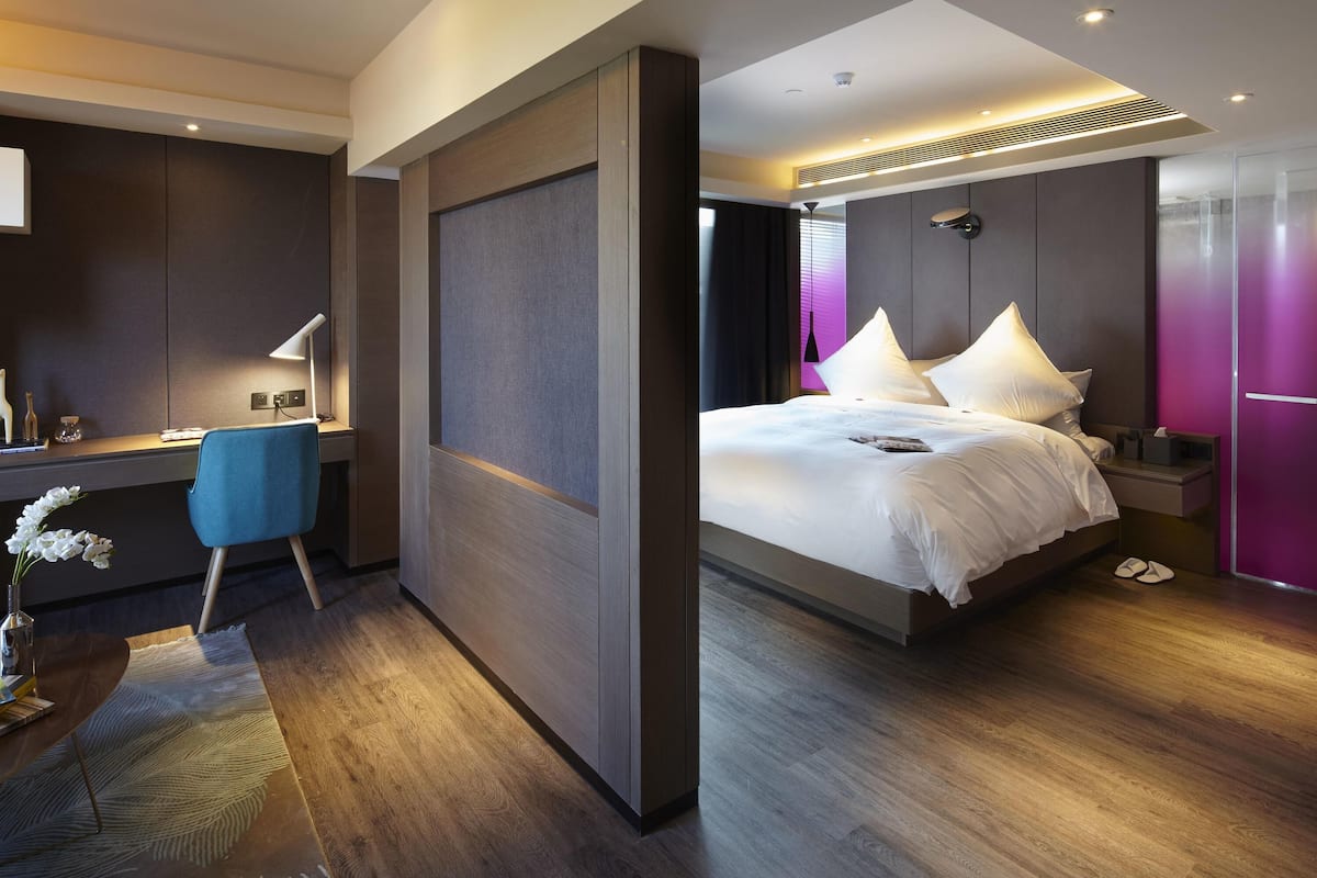 Ein modernes Hotelzimmer mit Schreibtisch, Stuhl, Bett und Blick auf die Stadt.