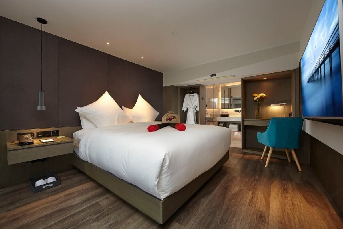 A modern hotel room with a large bed, bedside table, and a desk area.