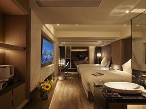 Ein modernes Hotelzimmer mit einem großen Bett, einem Schreibtisch, einem Fernseher und einem Badezimmer mit einem Marmorwaschbecken.
