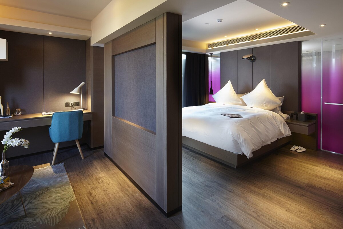Una habitación de hotel moderna con escritorio, silla, cama y vistas a la ciudad.