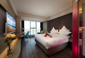 Una habitación de hotel moderna con una cama grande, un escritorio, una silla y un ventanal amplio.