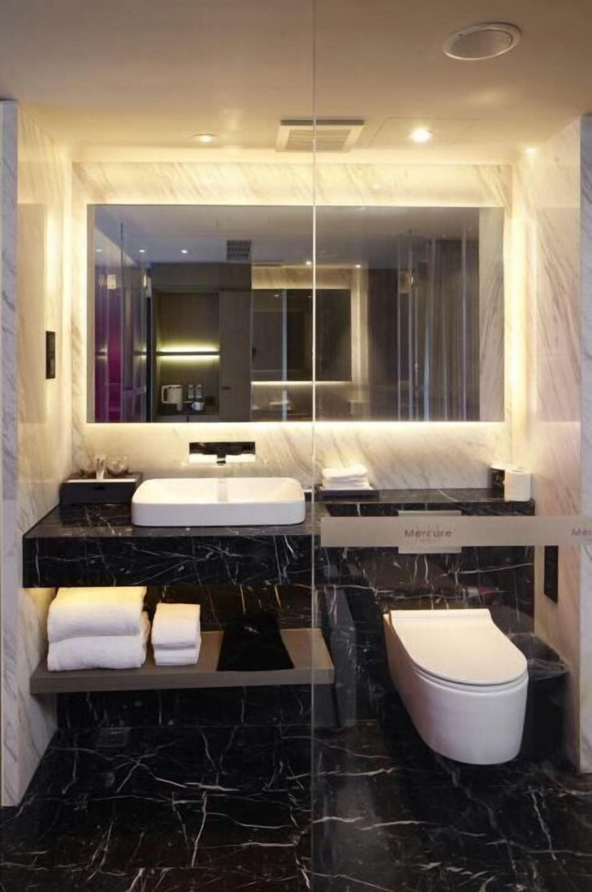 A modern bathroom with a large mirror, two sinks, a toilet, and marble flooring.