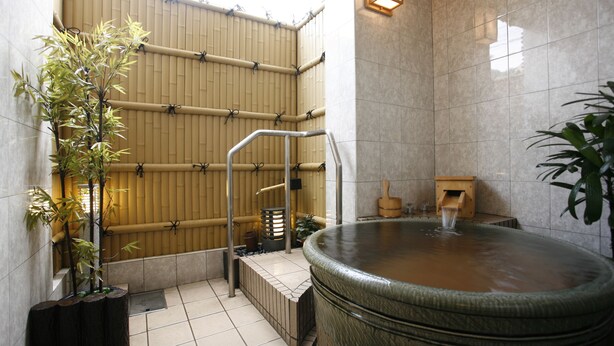 Un área de baño tradicional japonesa con una bañera amplia, pared de bambú y un banco de madera.