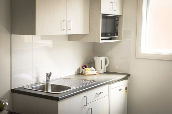 Una cocina moderna con un lavamanos de acero inoxidable, un microondas y un hervidor sobre la encimera.