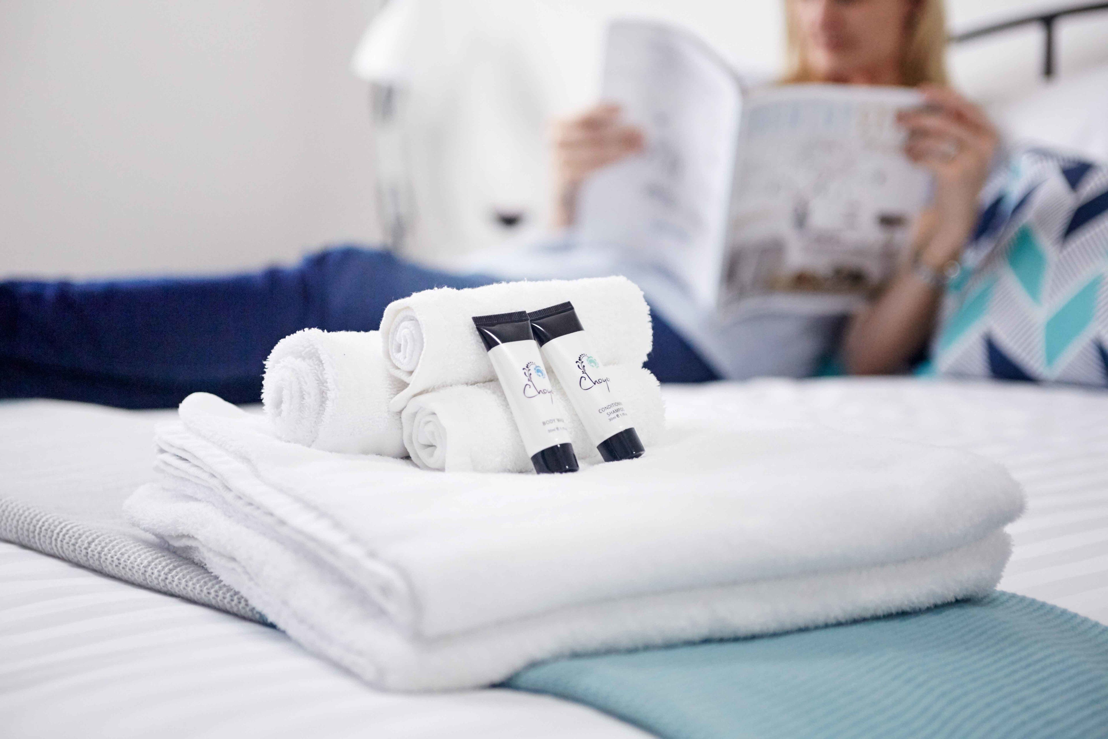Uma cama bem arrumada com toalhas brancas dobradas e dois frascos de shampoo e condicionador.
