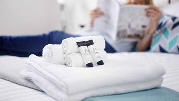Uma cama bem arrumada com toalhas brancas dobradas e dois frascos de shampoo e condicionador.