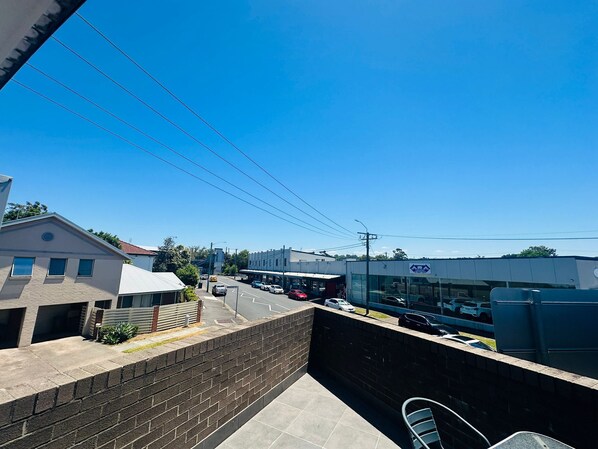 A balcony with a view of a street, buildings, and parked cars.