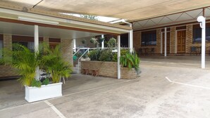 A covered outdoor area with potted plants, a brick wall, and a concrete floor. - Goomeri Motel (Goomeri)