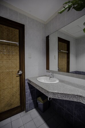 Un baño con lavamanos, espejo y puerta con toallero.