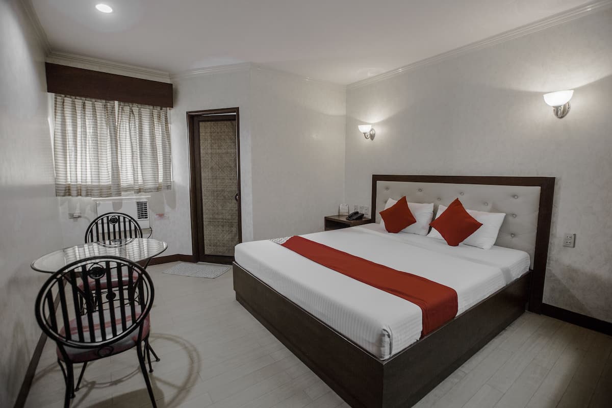Een hotelkamer met een groot bed, een klein tafeltje met stoelen en een raam met gordijnen.