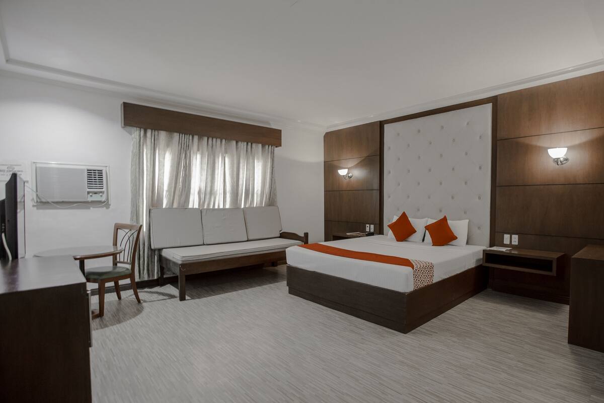 Een hotelkamer met een groot bed, een bureau, een stoel, een televisie en een raam met gordijnen.