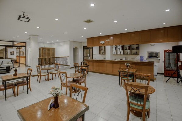 Un comedor amplio con múltiples mesas y sillas de madera, un área de cocina con armarios de madera y un espacio de estar con un sofá y una mesa de centro.