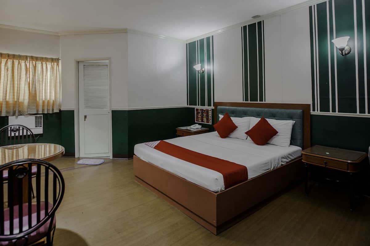 Een hotelkamer met een bed, nachtkastje, stoel en een klein tafeltje met een stoel.