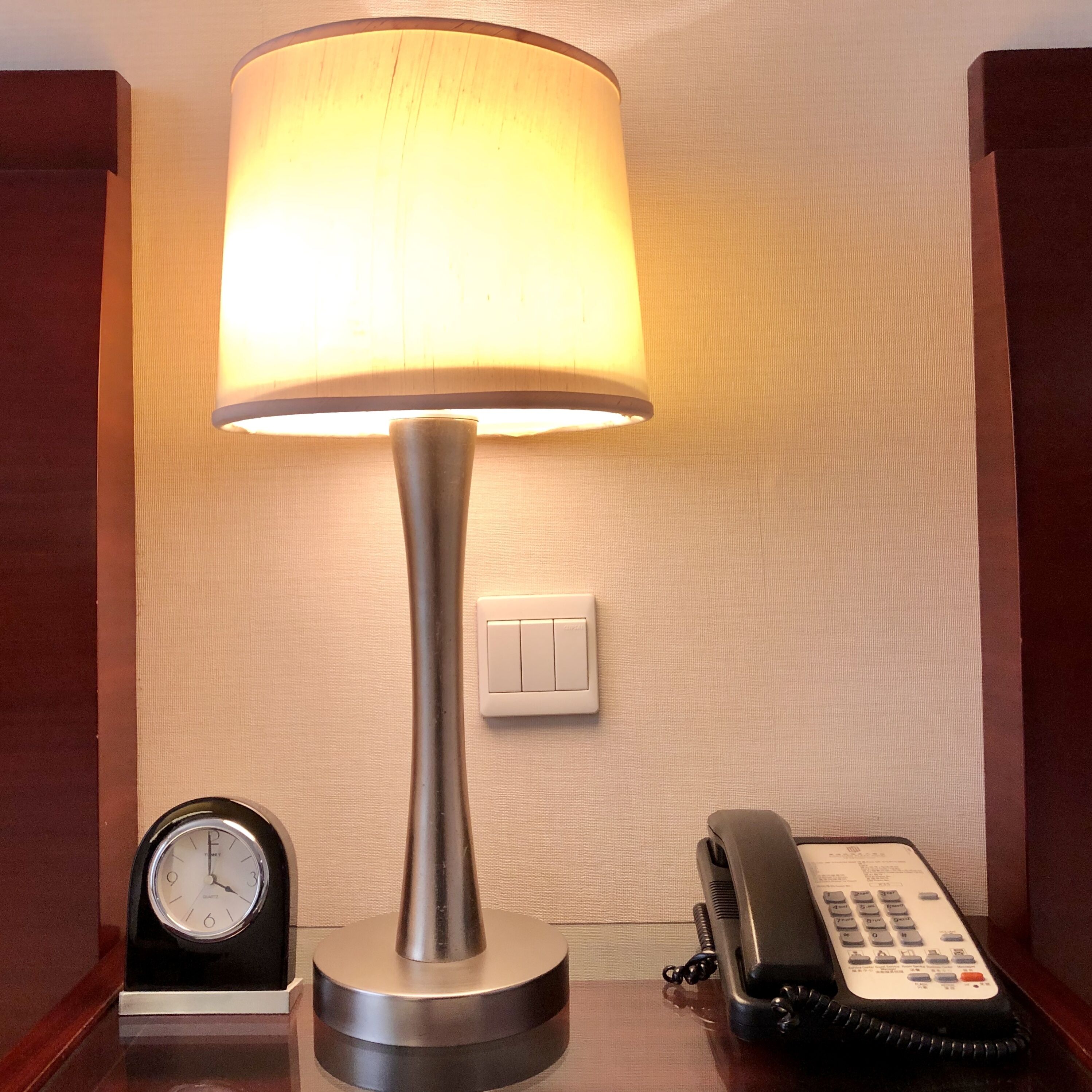 A lamp, a clock, and a telephone on a wooden surface.