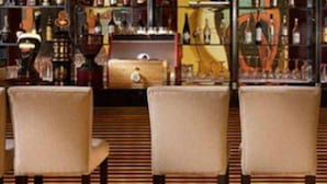 Un rincón de bar con varias botellas de licor, una pantalla de televisión y tres sillas.