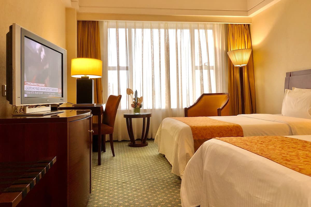 Habitación de hotel con dos camas, un escritorio, un televisor, una lámpara y una ventana con cortinas.