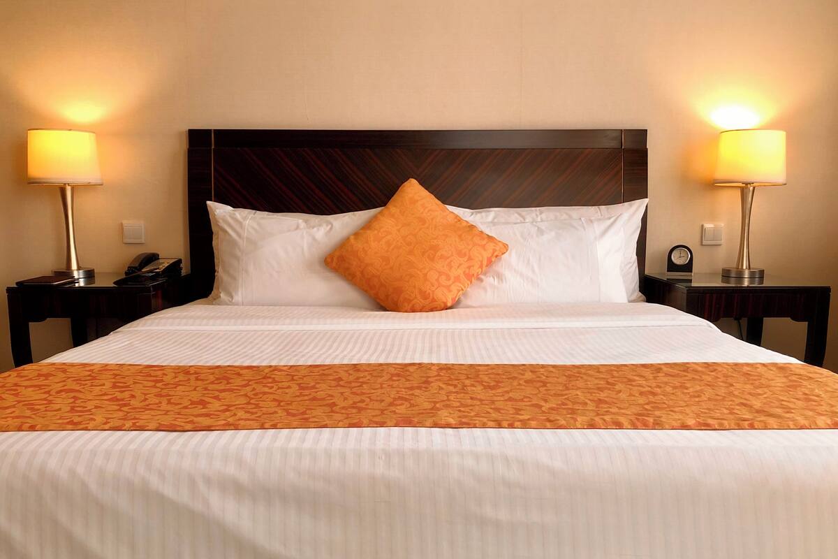 Habitación de hotel con una cama grande, dos lámparas de noche, un reloj y un teléfono en la mesita de noche.