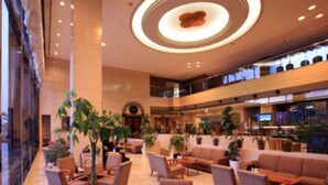 A spacious lobby with multiple seating areas, a central circular light fixture, and a large window providing natural light.