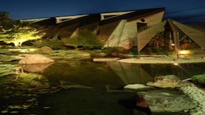 A modern building with a unique triangular roof design, surrounded by a tranquil pond and well-maintained landscaping.