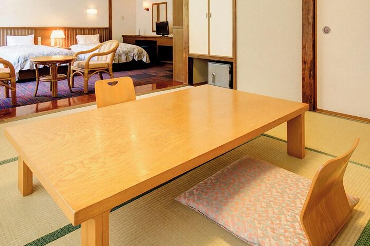 A traditional Japanese-style room with tatami flooring, a wooden table, a bed with a low headboard, and a desk with a chair.