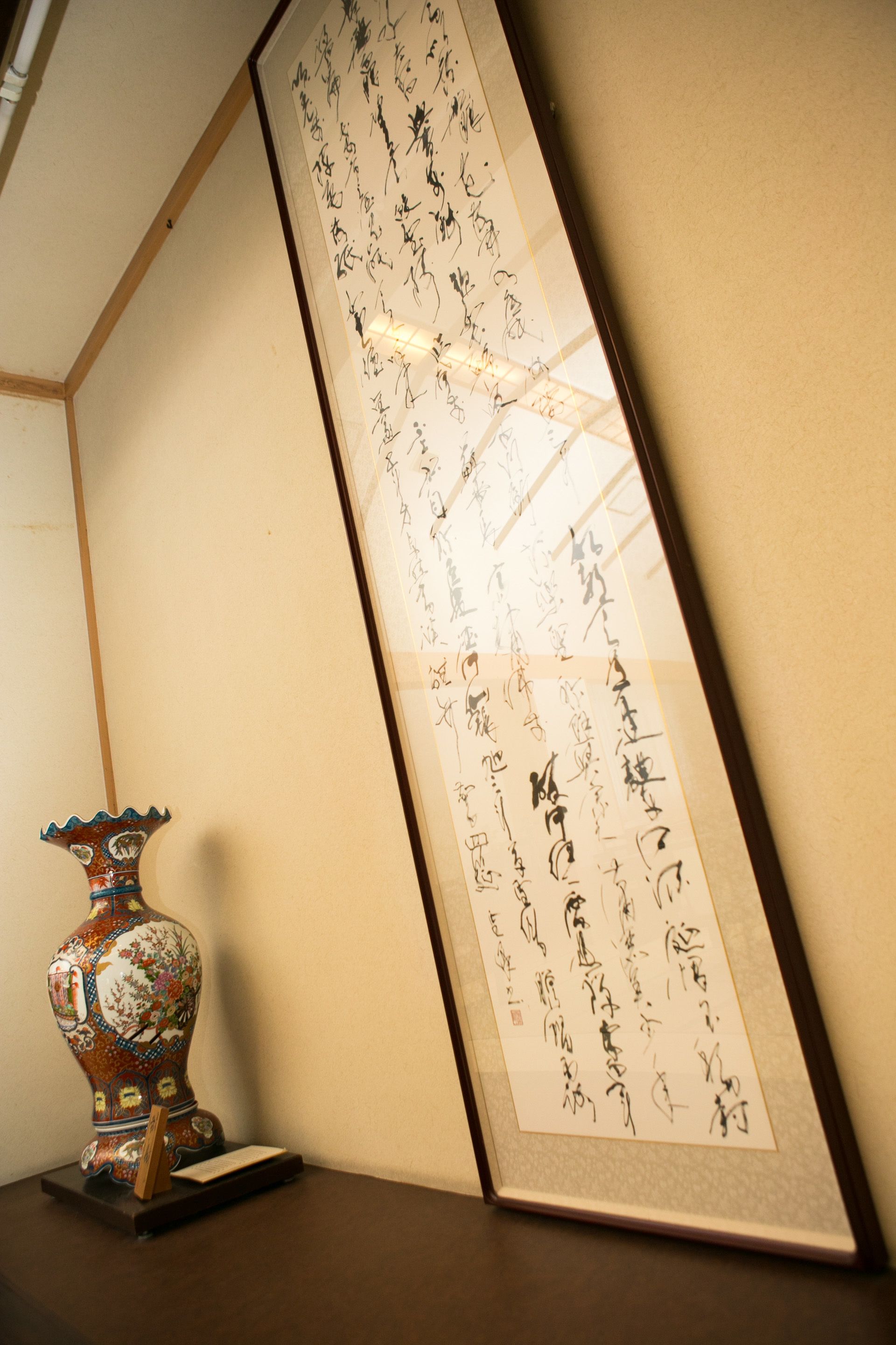 A framed calligraphy piece on a wall, a decorative vase, and a small table with a book.