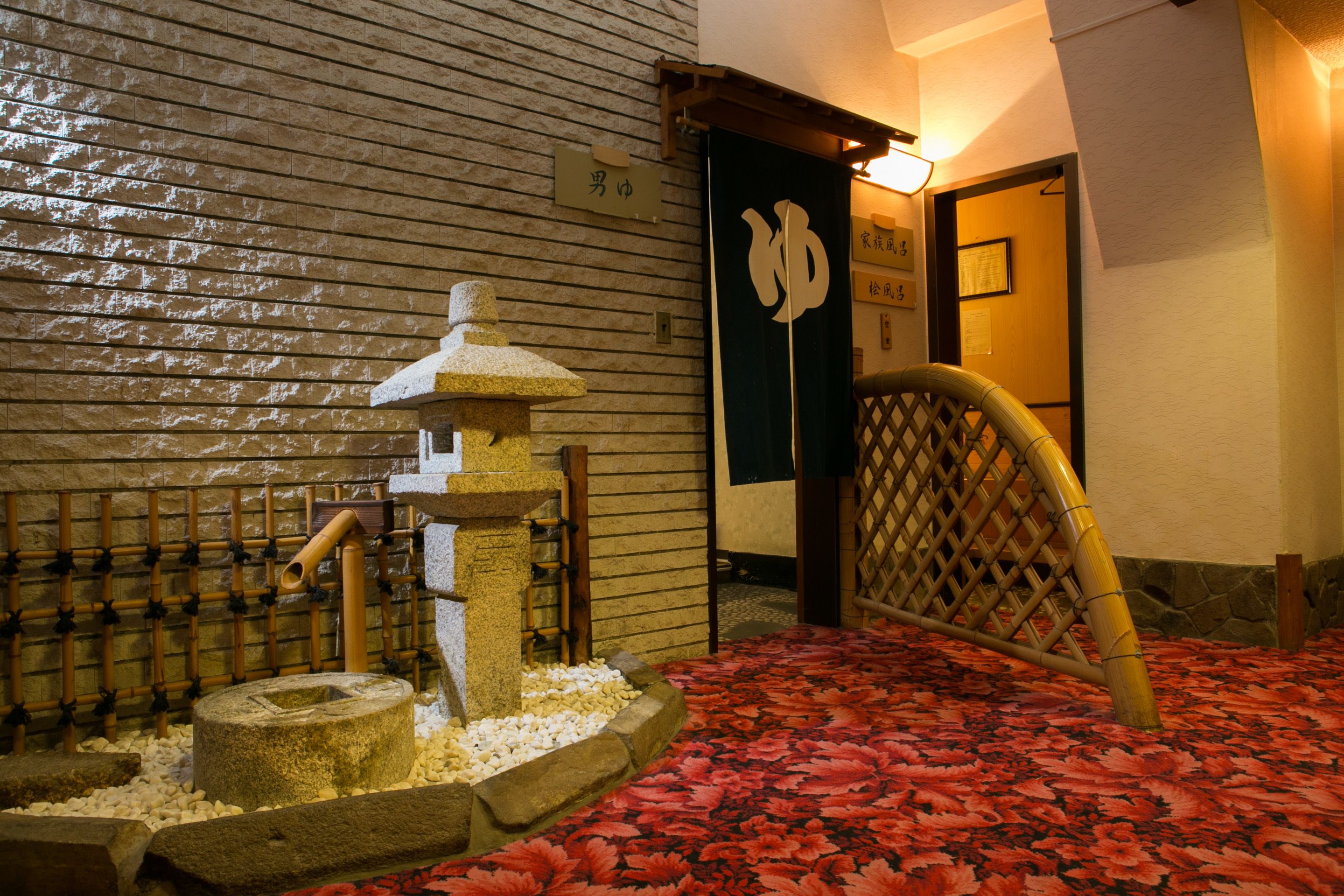 A traditional Japanese interior with a stone lantern, bamboo wall, and a red patterned floor.