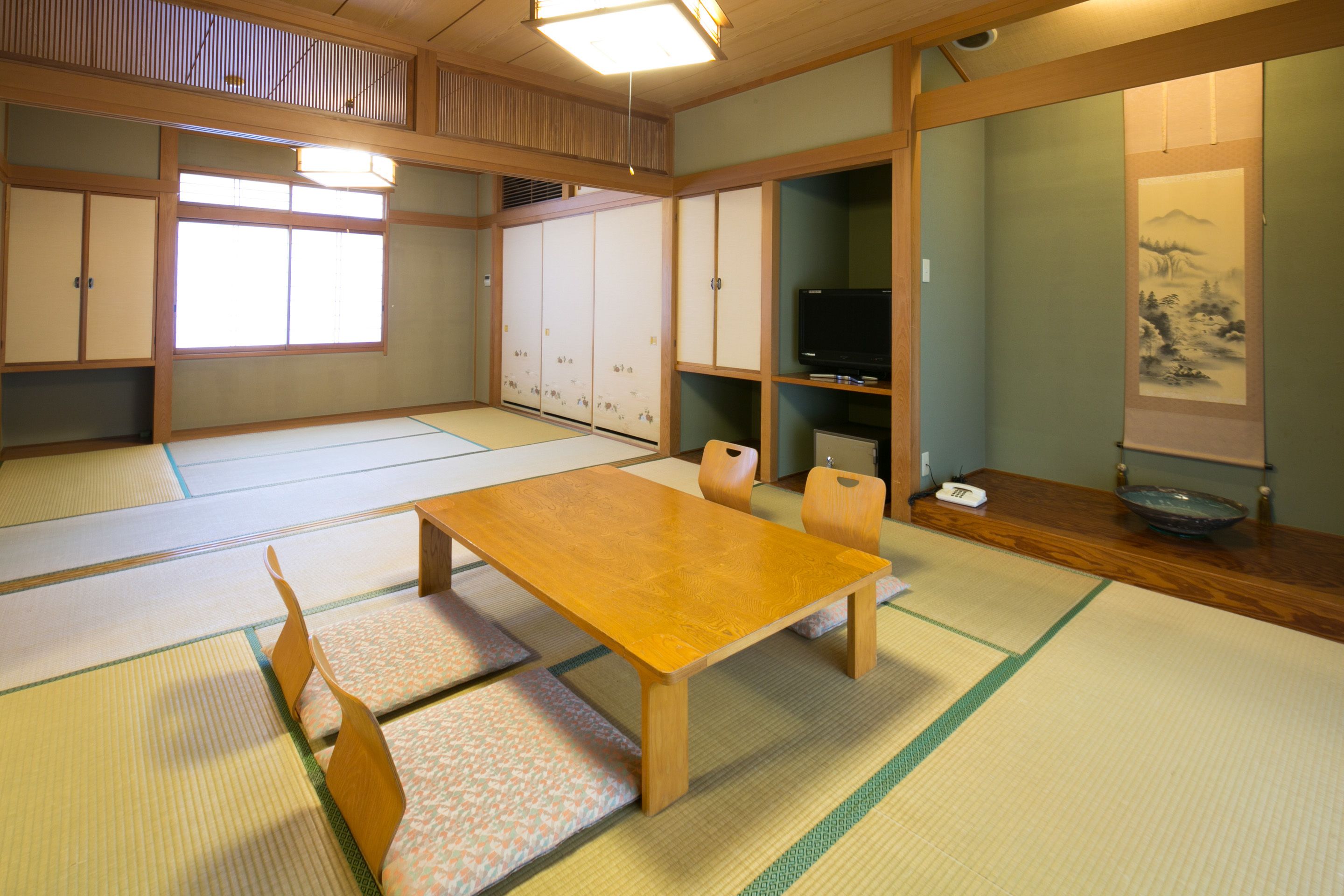 A traditional Japanese room with tatami flooring, a wooden table, tatami mats, a television, and sliding doors.