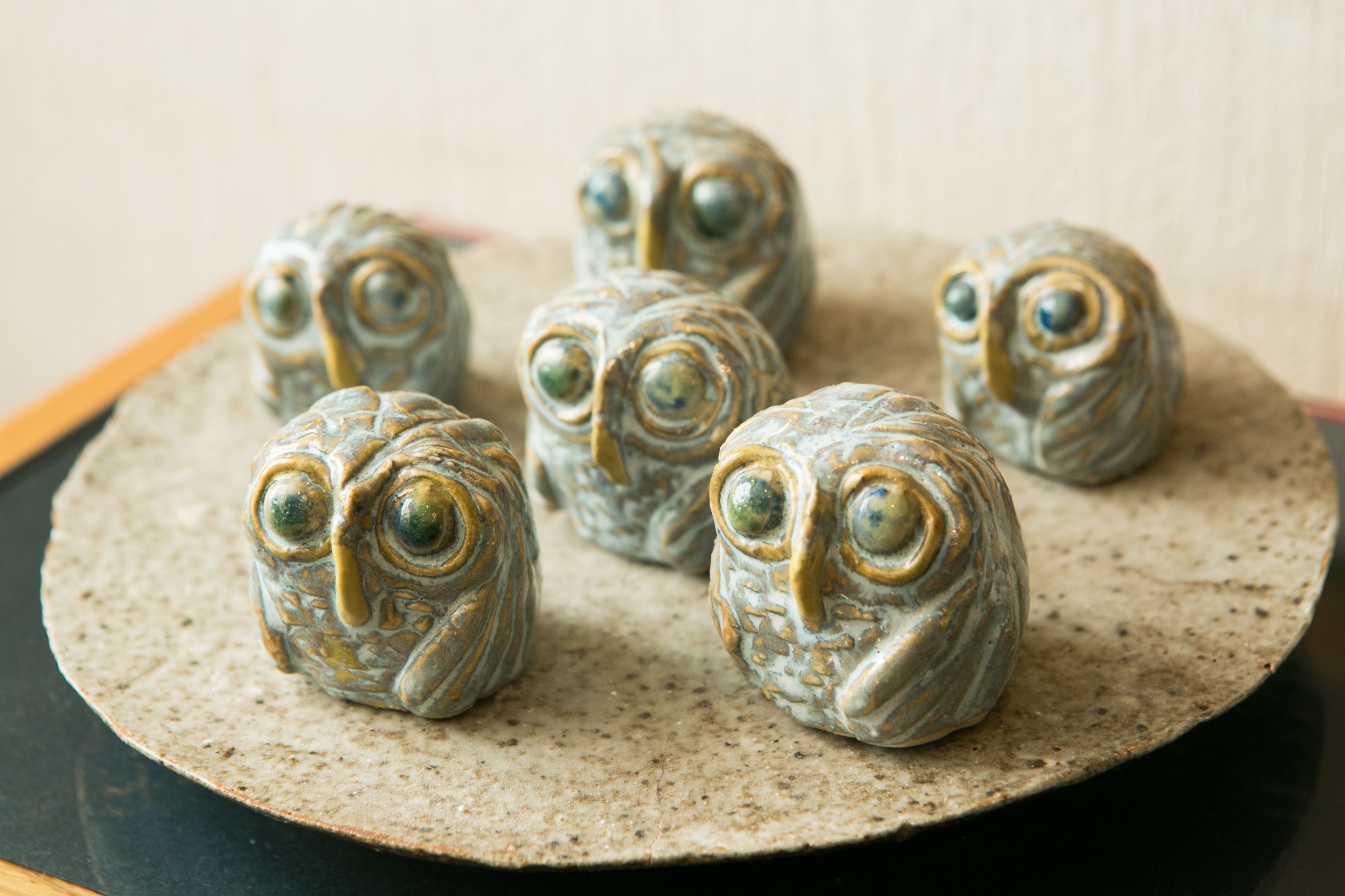 Five ceramic owl figurines on a round, speckled ceramic plate.
