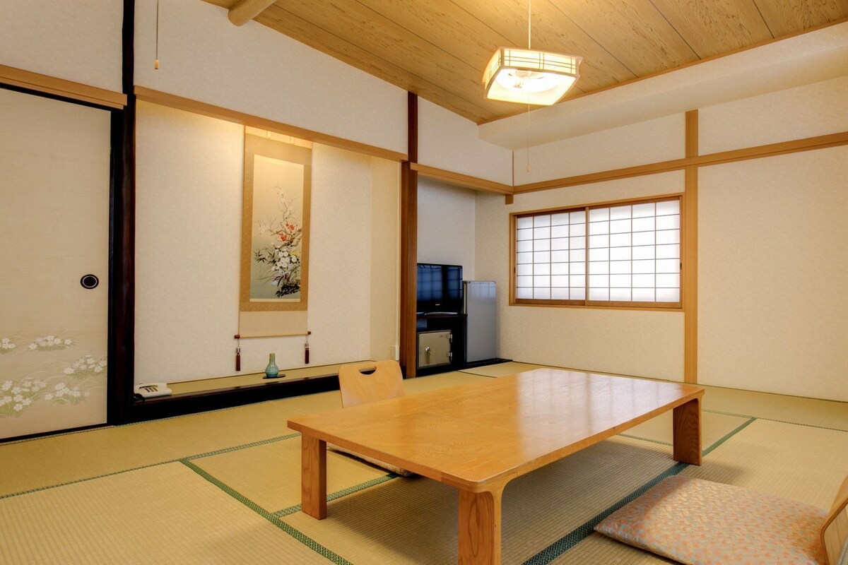 A traditional Japanese room with tatami flooring, a low wooden table, a television, and a shoji screen.