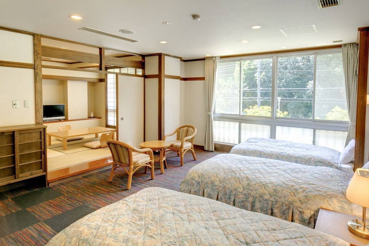 A hotel room with two beds, a desk with a chair, a television, and a large window.