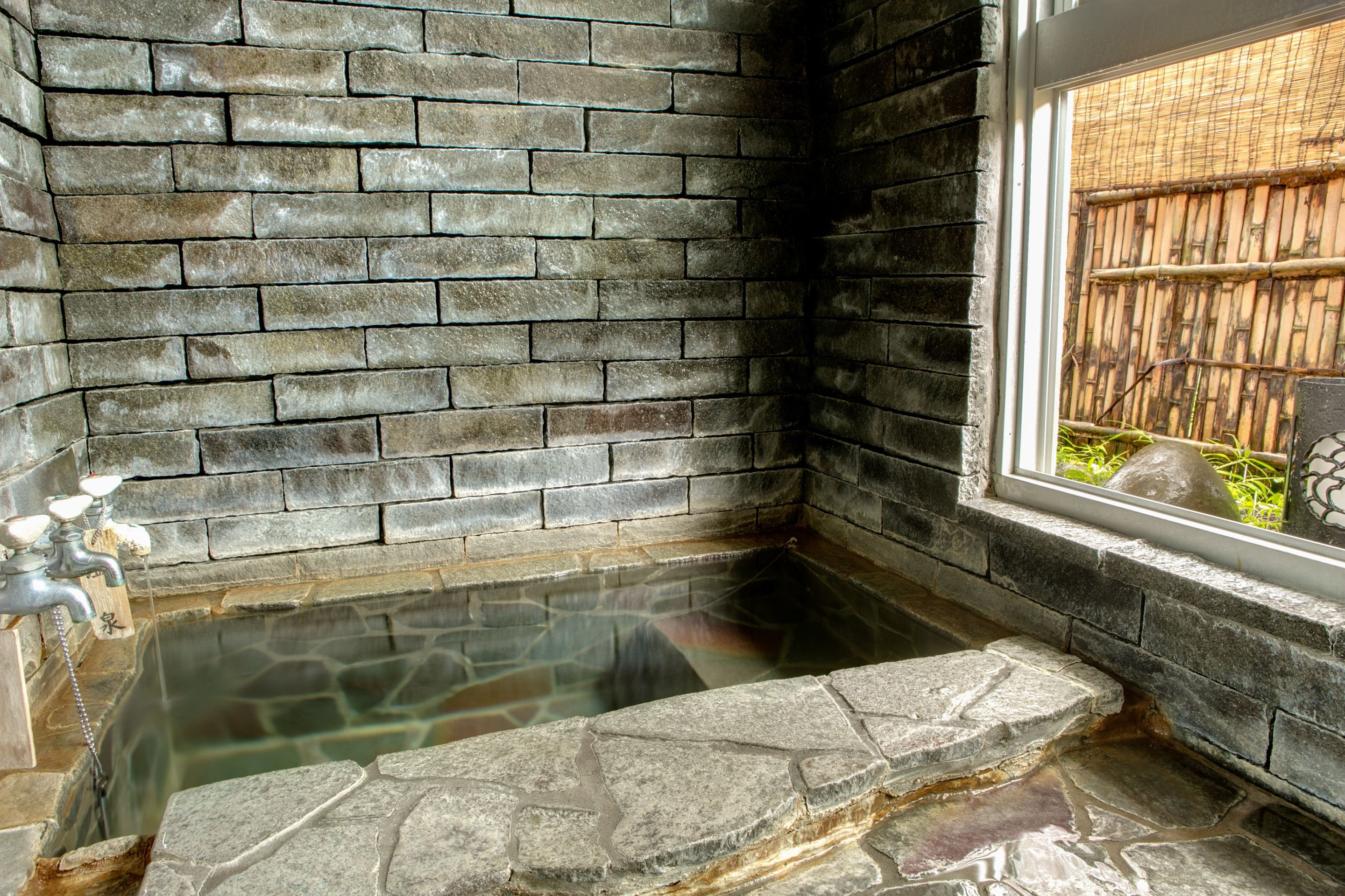 A stone hot tub with a brick wall backdrop and a window view.