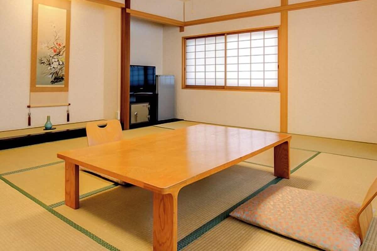 Ett traditionellt japanskt rum med tatamimattor på golvet, ett lågt träbord, en skjutdörr och utsikt genom en shojiskärm.