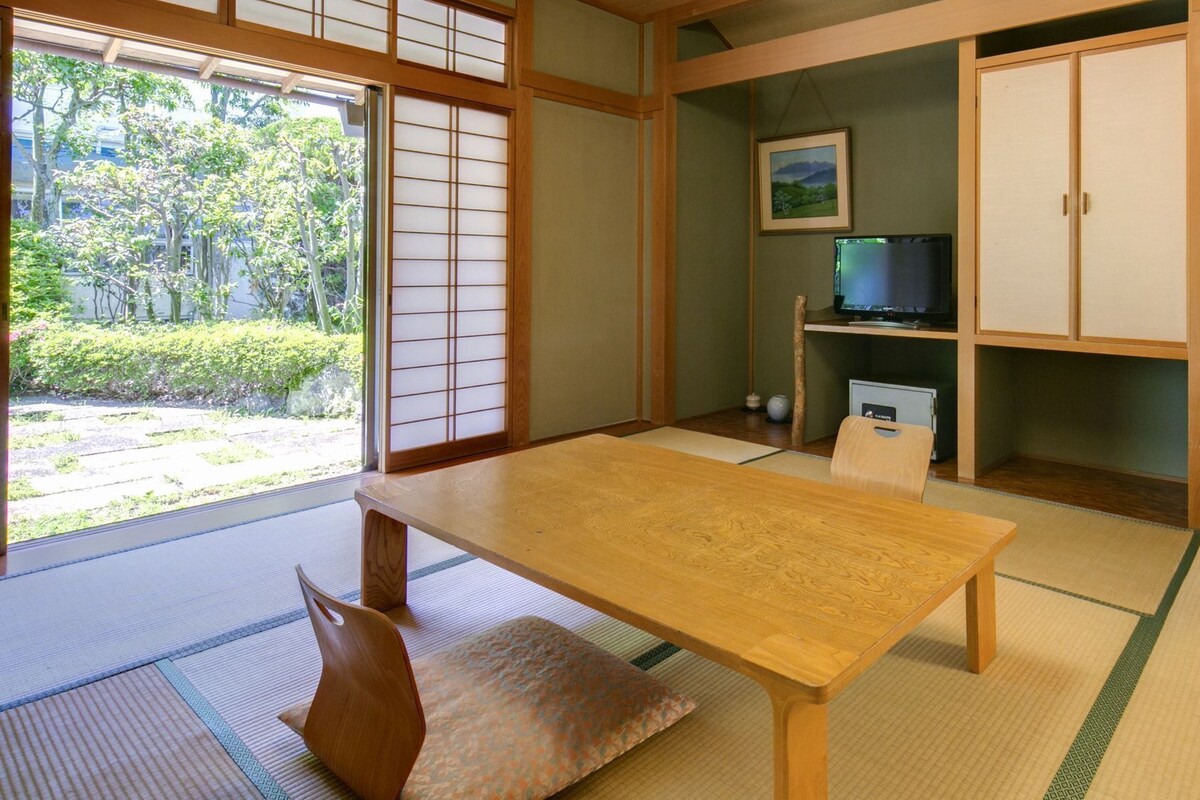 A traditional Japanese room with tatami flooring, a wooden table, a television, and a cabinet.