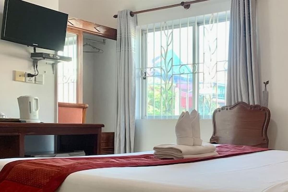 Habitación de hotel con cama, televisión montada en la pared, escritorio con silla y ventana con cortinas.