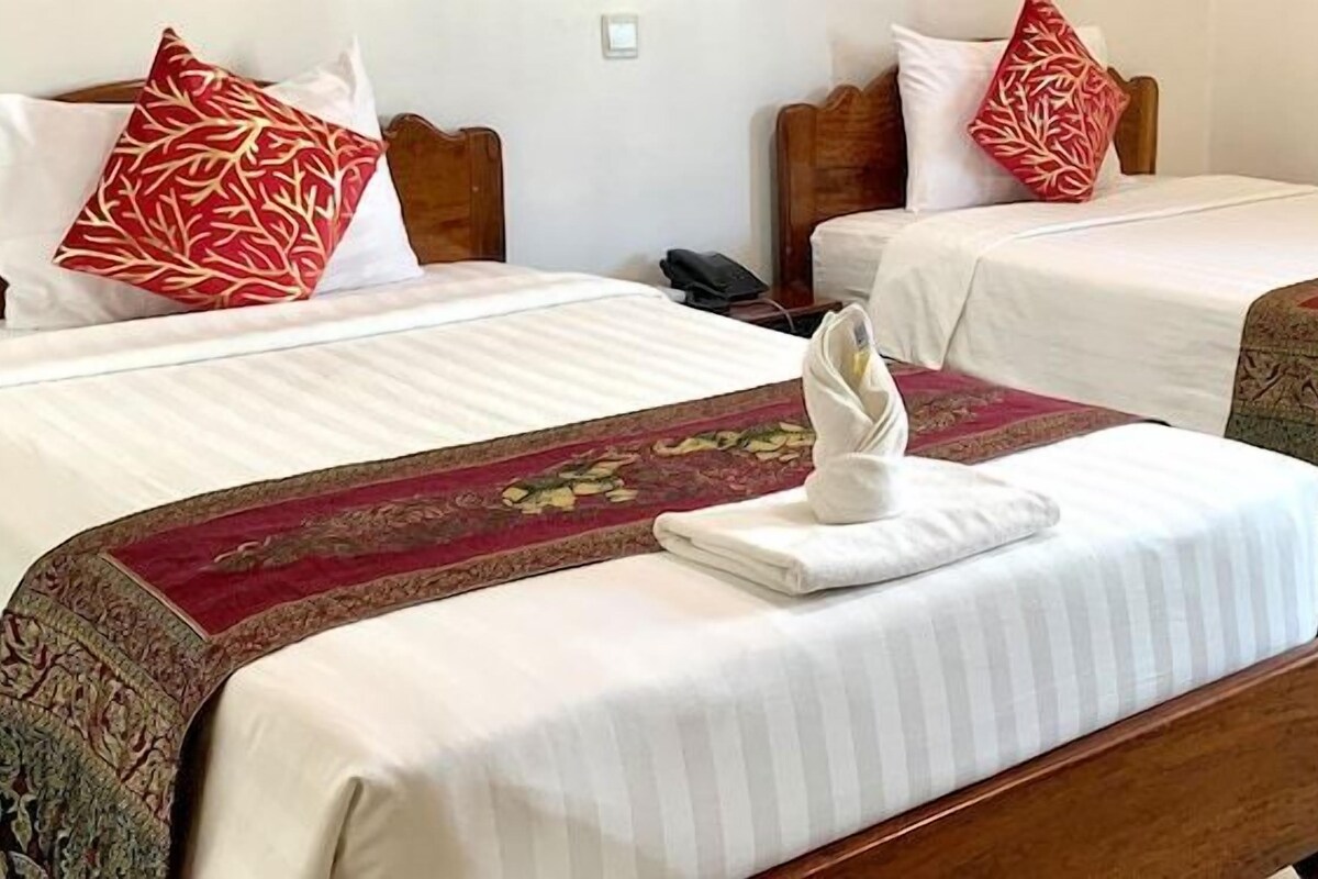 Habitación de hotel con dos camas individuales, cada una con almohada de estampado rojo y blanco, una manta blanca y una toalla doblada sobre la cama.