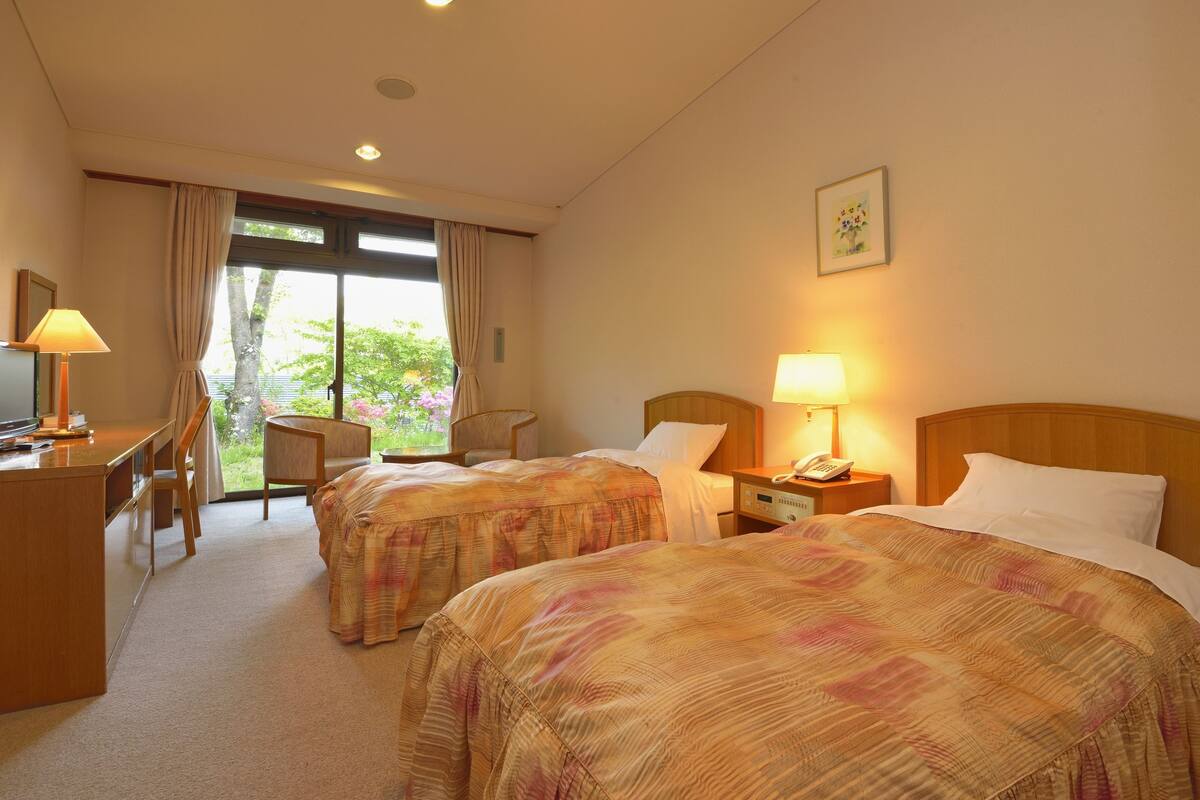 A hotel room with two beds, a desk, a chair, and a window with curtains.