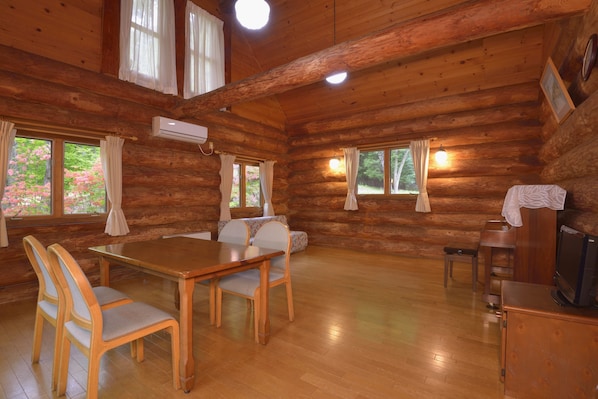 Interior de una cabaña de troncos con una mesa de comedor de madera, sillas, un televisor y una chimenea.