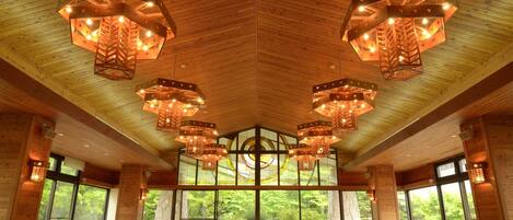 Una sala conferenze ampia con lunghe tavolate e sedie, soffitto in legno e ampie finestre con vista sugli alberi.