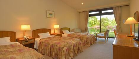 A hotel room with two beds, a desk, a chair, and a window with a view of greenery.