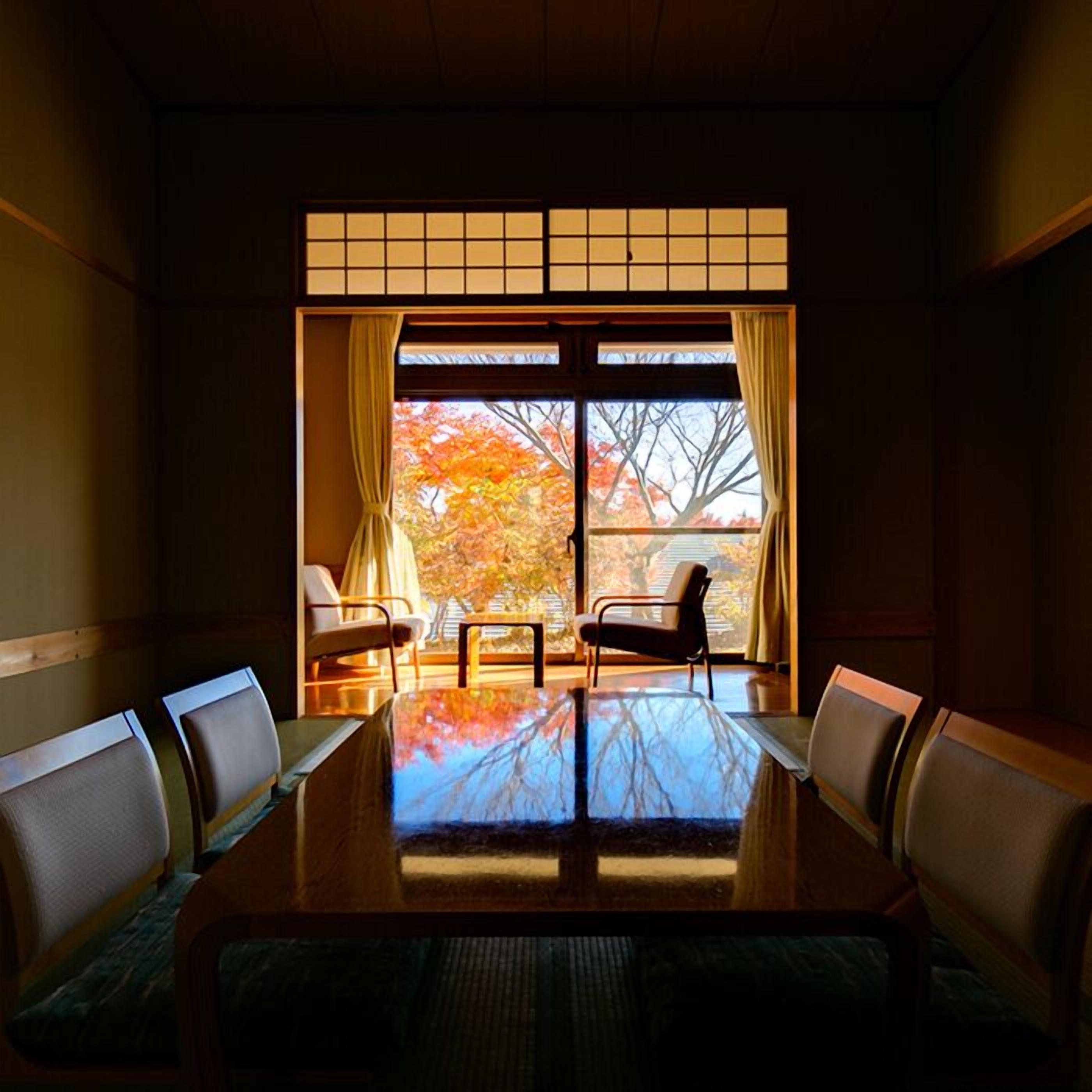 A traditional Japanese room with tatami flooring, a low table, and sliding doors with a view of autumn trees.